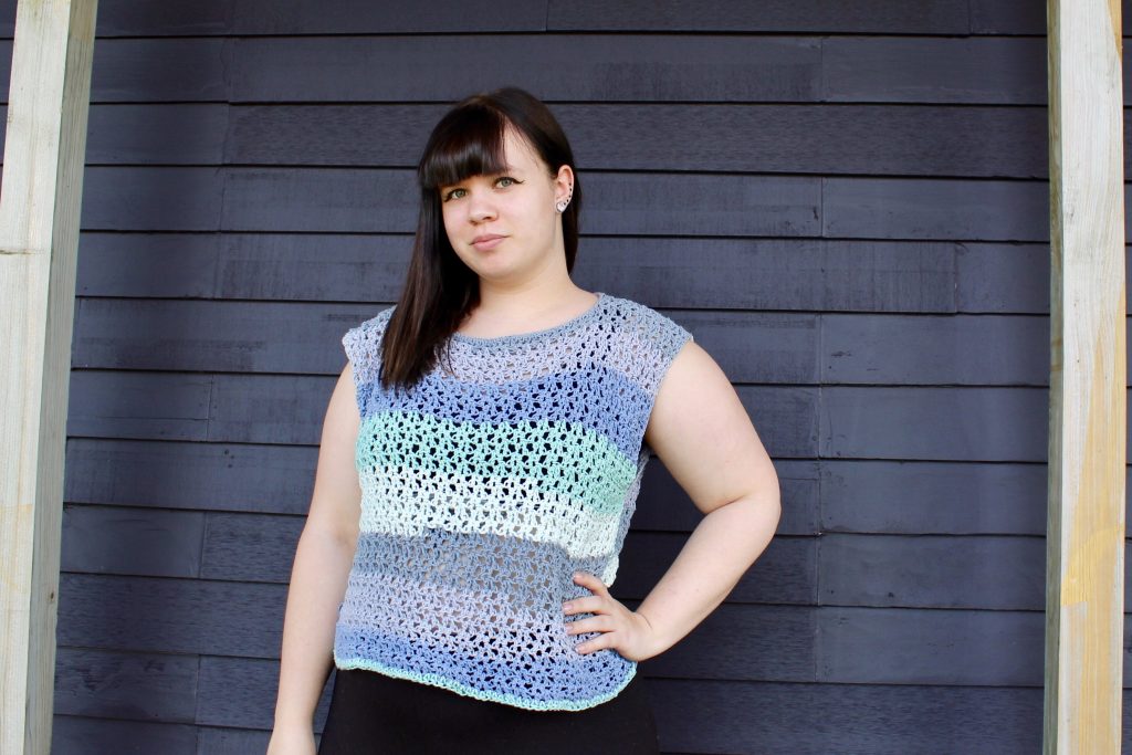 Evelyn wearing the Tanabota Top, a loose crochet striped top. The top has an open weave and is in blues and teals.