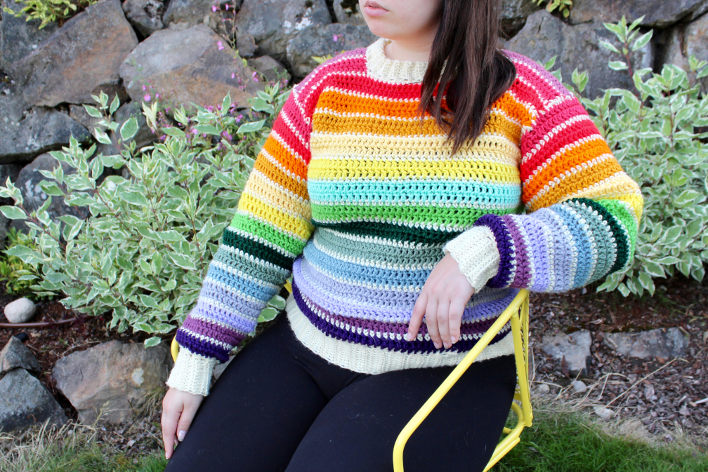 Evelyn is sitting down wearing a rainbow crochet sweater